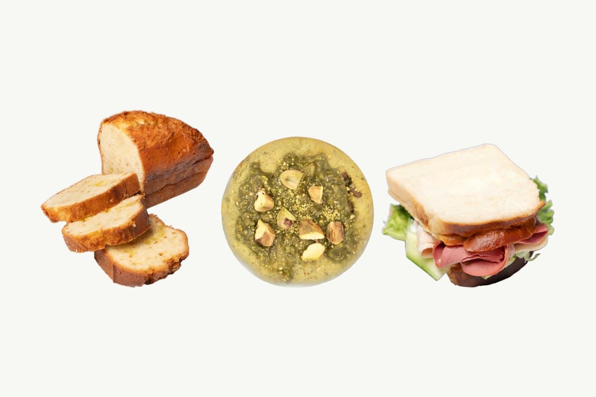 A Classic Lemon Butter Cake Loaf with three slices cut, a Pistachio Chocolate Chip Cookie and a White Bread Smoked Turkey Sandwich in a row on a plain cream background