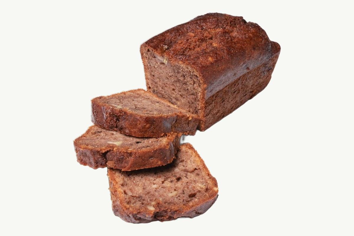 Banana and pecan cake loaf sliced on a plain cream background