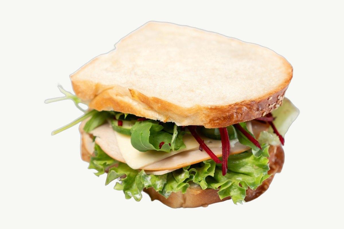 A brioche smoked chicken sandwich with lettuce, cheese and beetroot slaw on a plain cream background