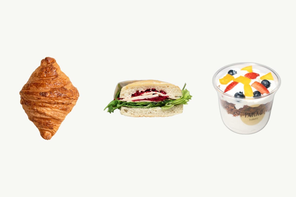 A plain butter croissant, a ciabatta turkey and cheese sandwich and a granola parfait cup on a plain cream background