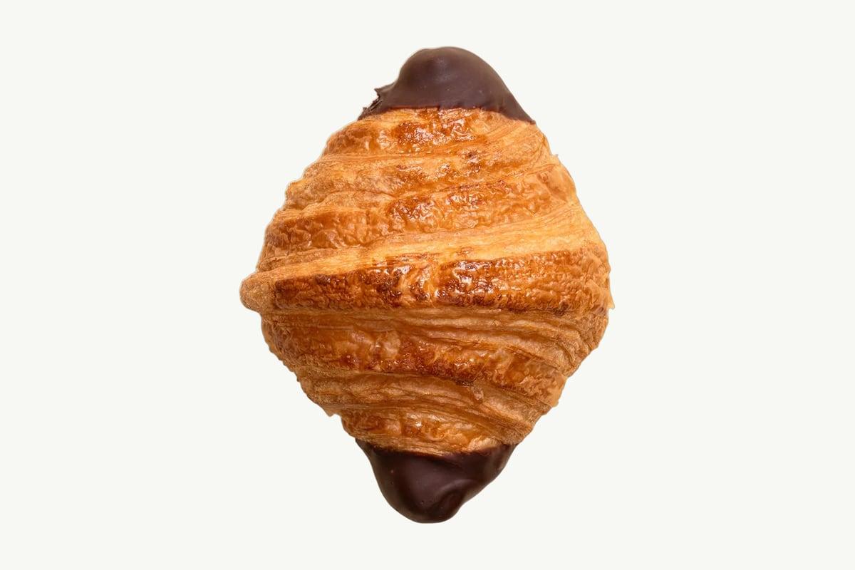 A chocolate-dipped croissant resting on a plain cream surface, glaze still glossy