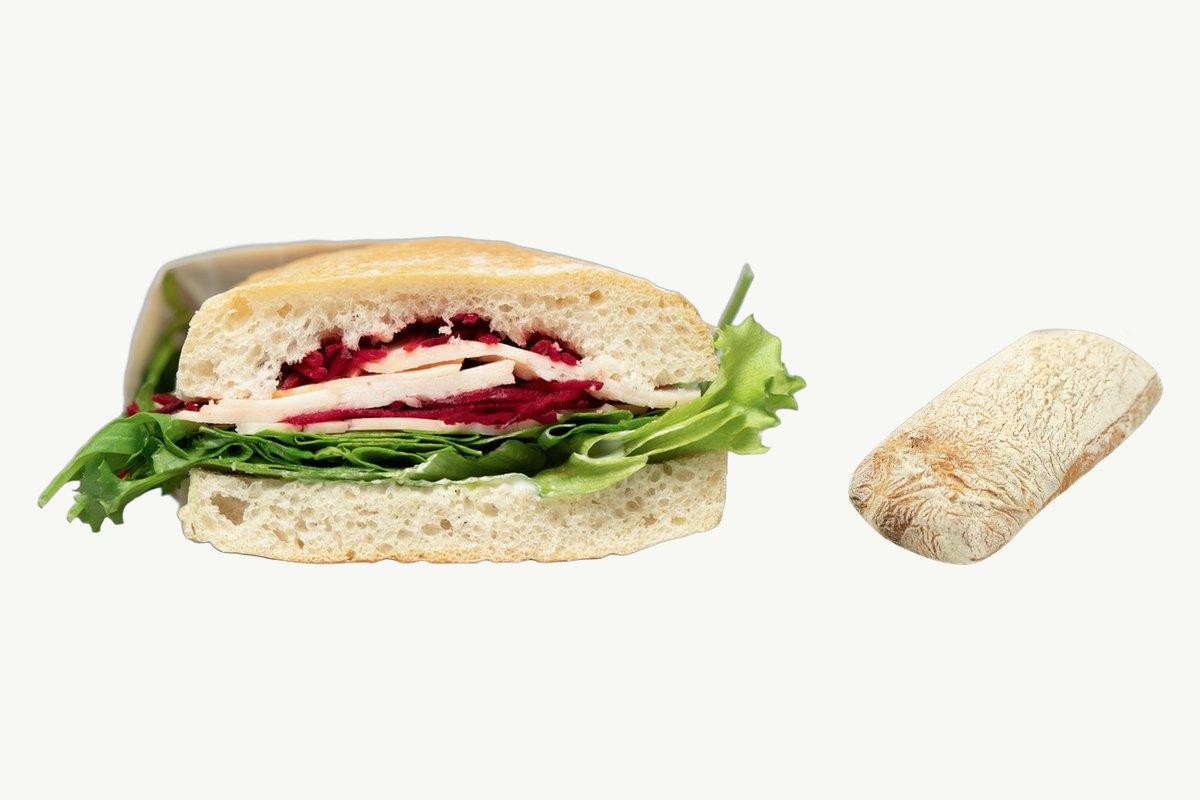 A ciabatta turkey and cheese sandwich beside a whole sourdough ciabatta on a plain cream background