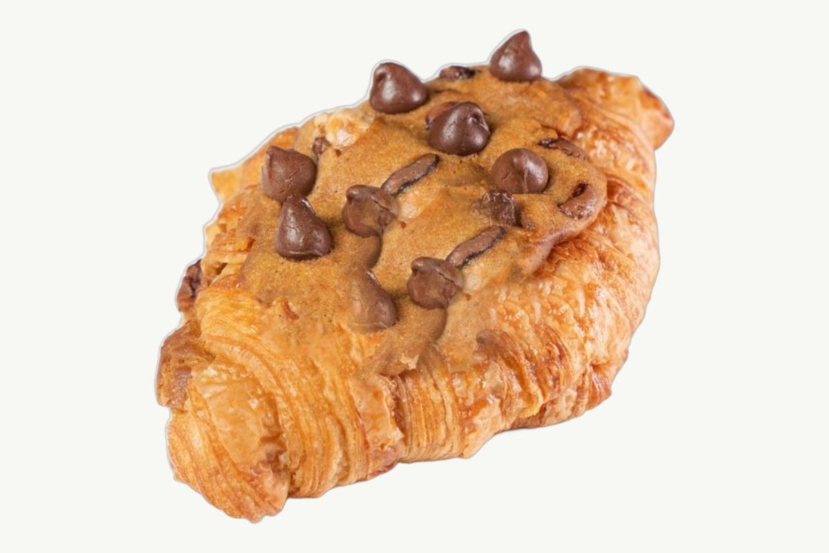 Cookie croissant topped with baked cookie dough on a plain cream background