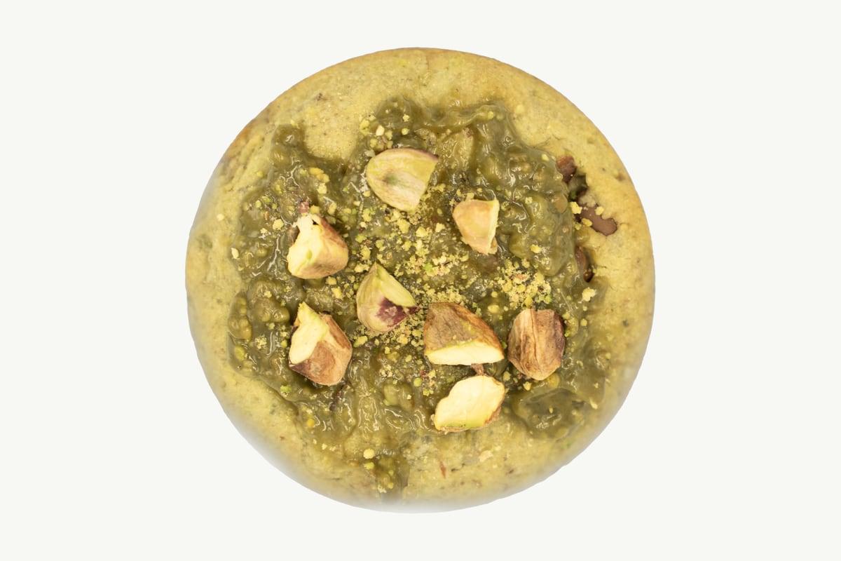 Thick pistachio cookie topped with chopped pistachios on a plain cream background