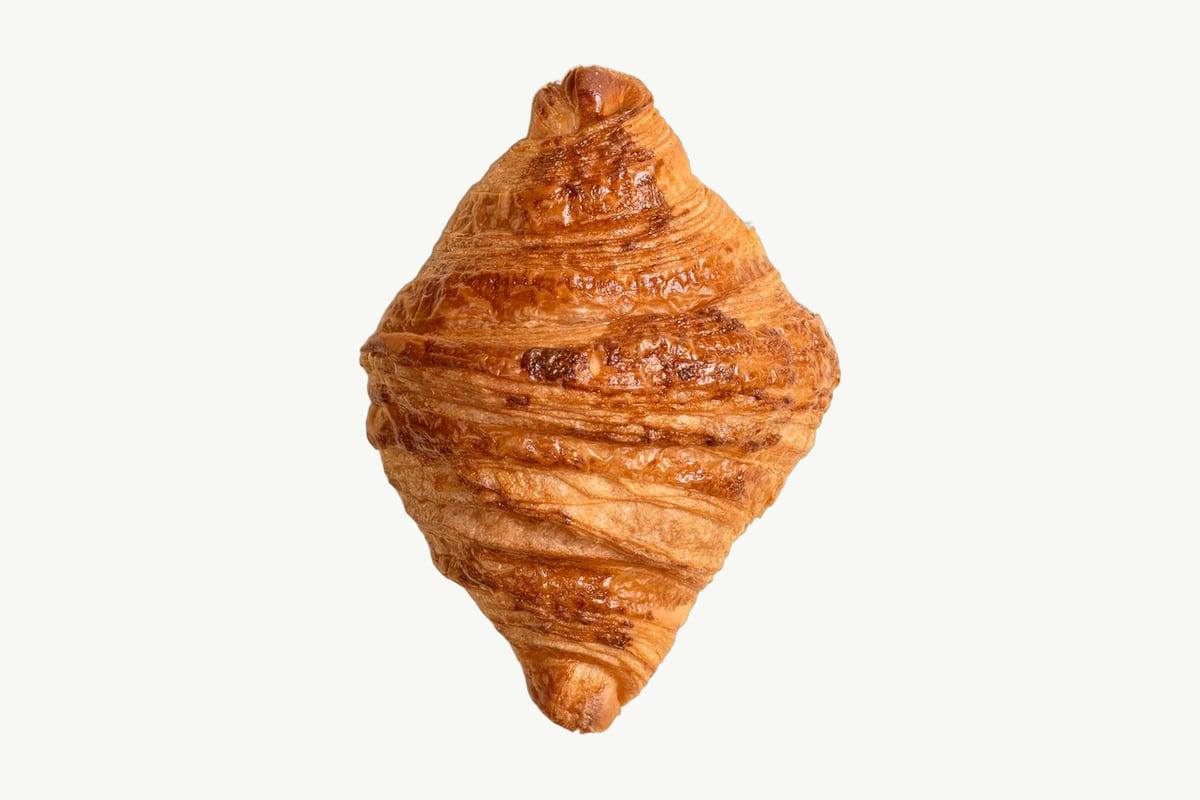A golden layered butter croissant resting on a plain cream background