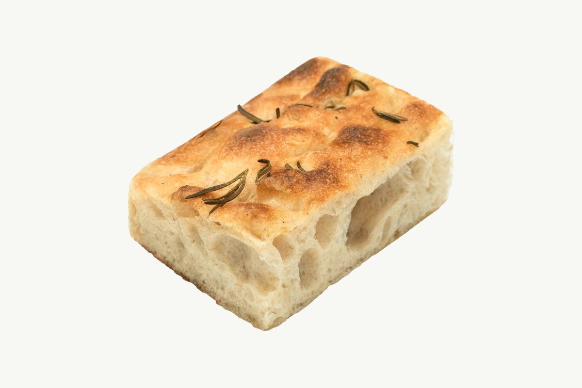 A single square of rosemary focaccia shot from above on a plain cream background