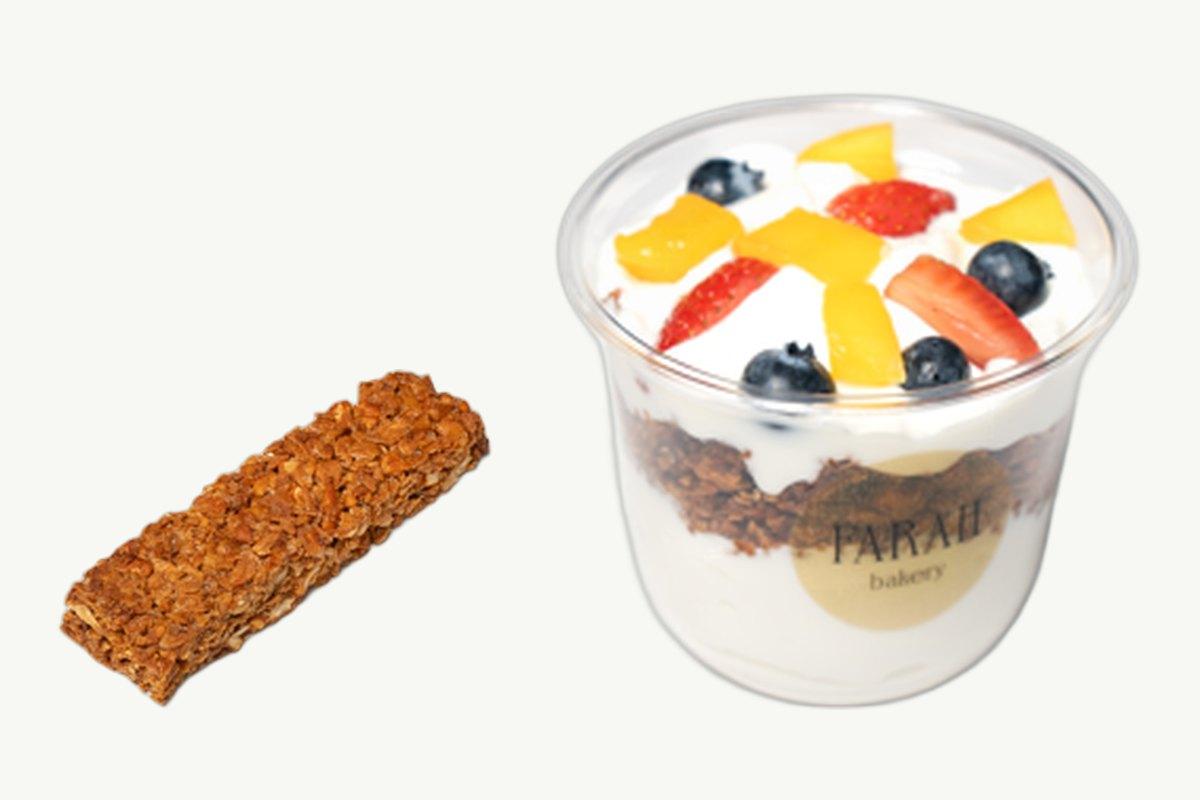 A baked granola bar beside a granola parfait cup topped with fresh fruit on a plain cream background