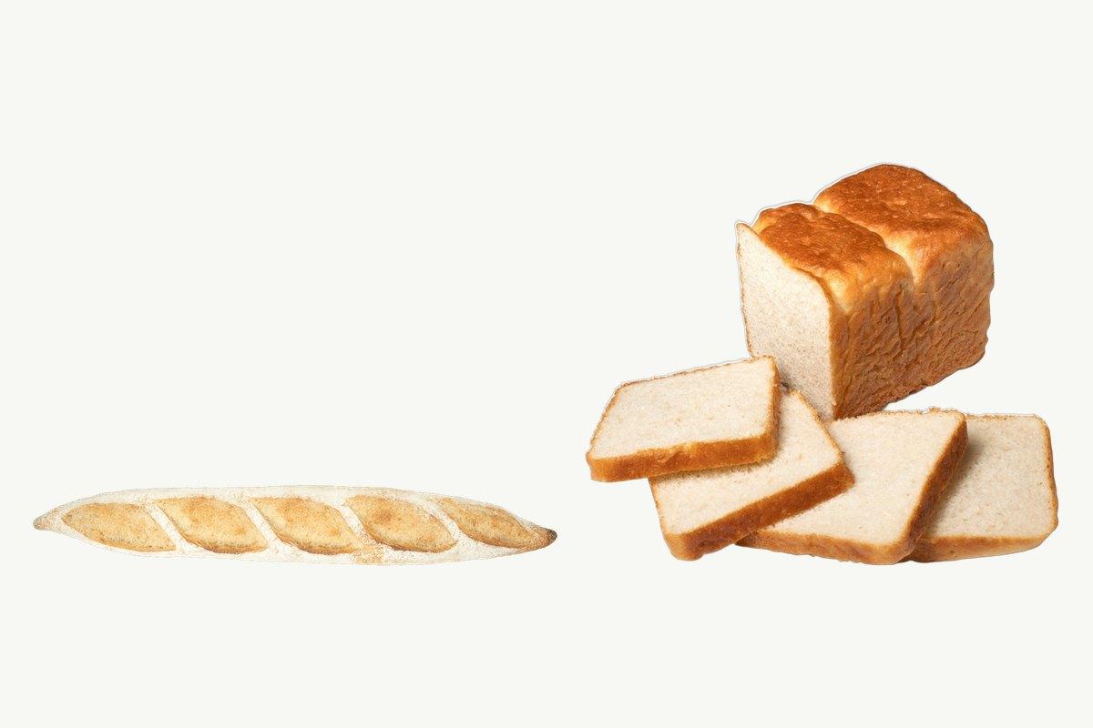 A sourdough baguette lying beside a sliced white toast loaf on a plain cream background