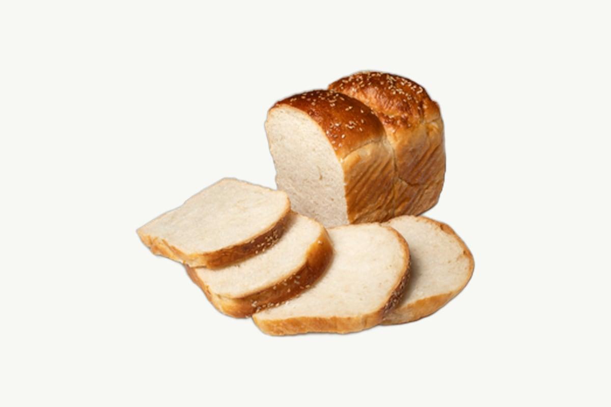 A pale golden Japanese milk bread loaf resting on a plain cream background