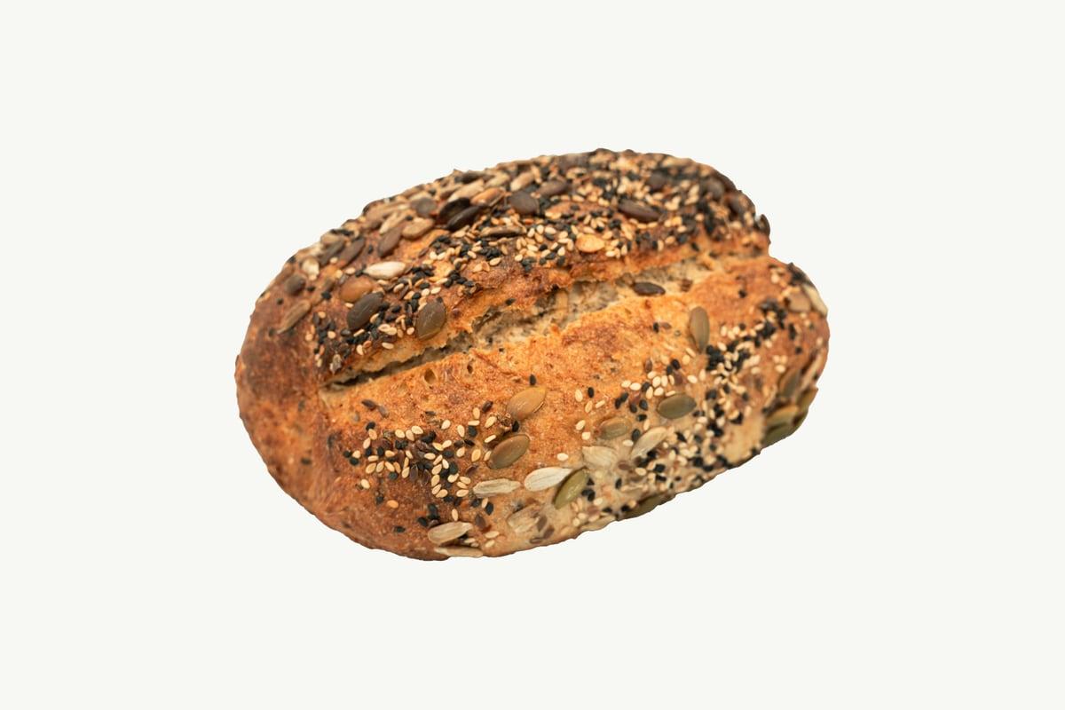 A seeded multi-grain sourdough loaf resting on a plain cream background