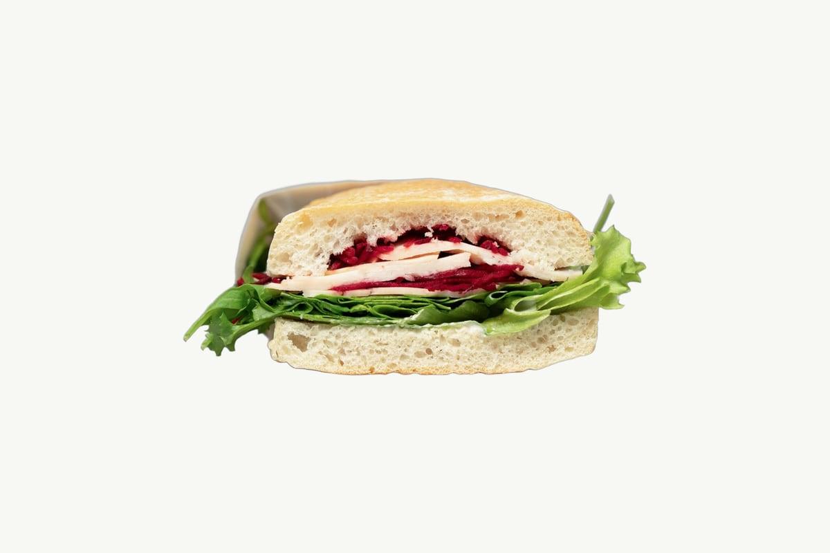 Ciabatta turkey and cheese sandwich cut open on a plain cream background