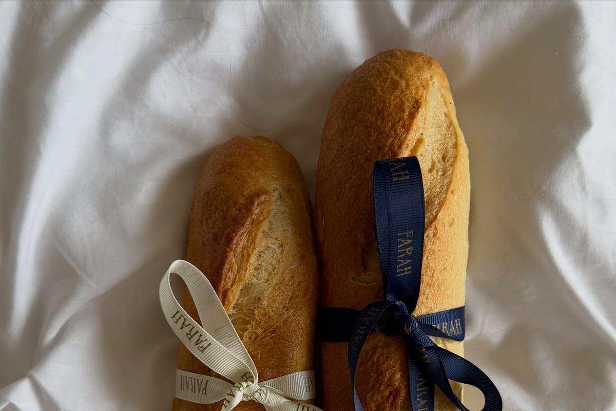 Two golden baguettes tied with cream and navy ribbons on white linen