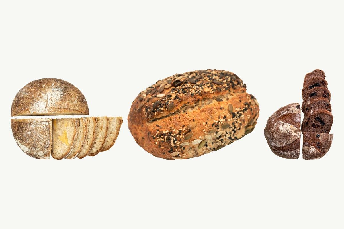 A halved and sliced sourdough cheese loaf, a multi-seed sourdough and a halved chocolate sourdough on a plain cream background
