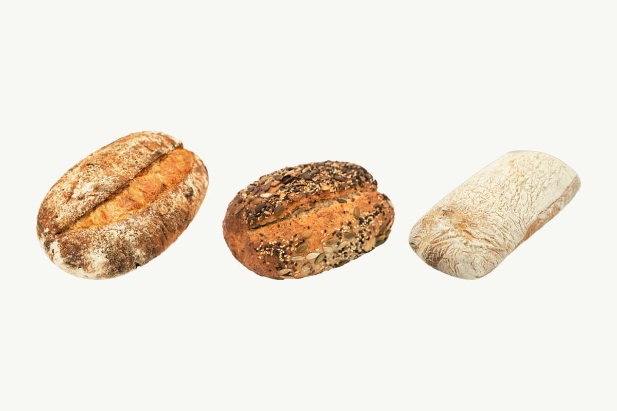 A country sourdough loaf, a multi-seed sourdough loaf and a sourdough ciabatta side by side on a plain cream background