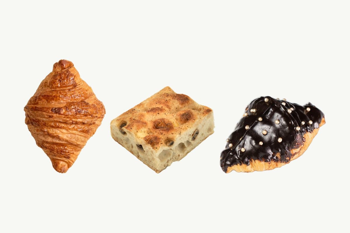 A plain croissant, a square of mushroom focaccia and a chocolate croissant in a row on a plain cream background