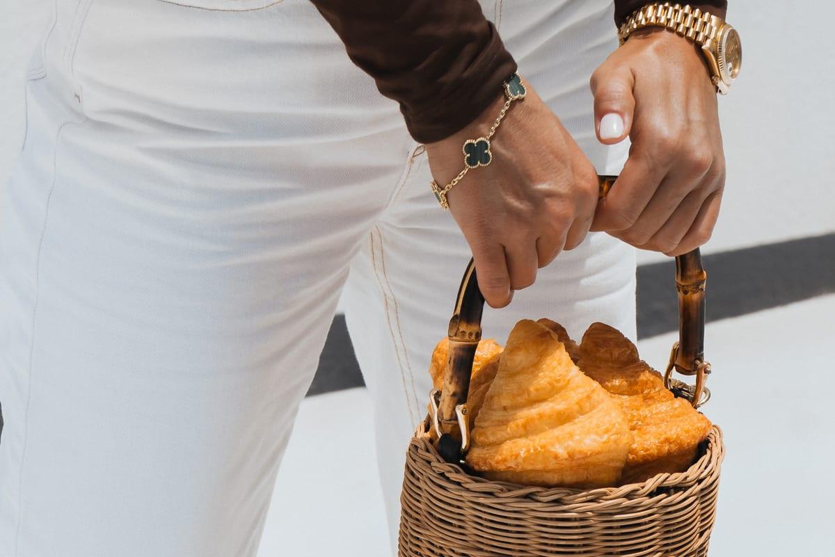 Hand carrying a wicker basket of golden croissants against a bright white wall