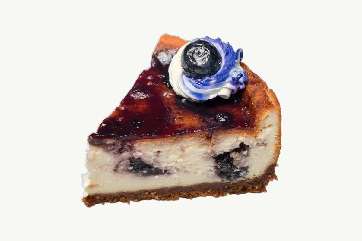 Slice of blueberry cheesecake with fruit topping on a plain cream background