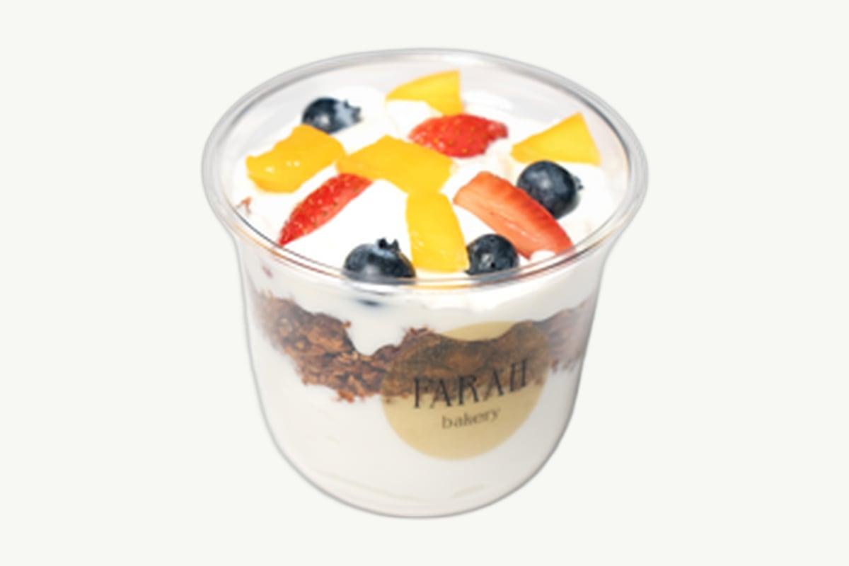 Layered granola and Greek yoghurt parfait in a glass on cream background