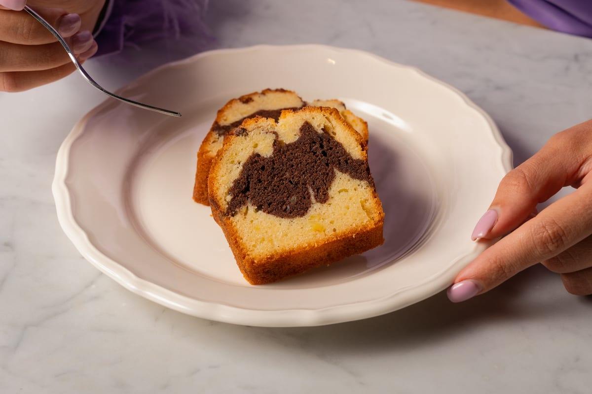 Slice of marble cake with dark chocolate swirl on a white plate, marble tabletop