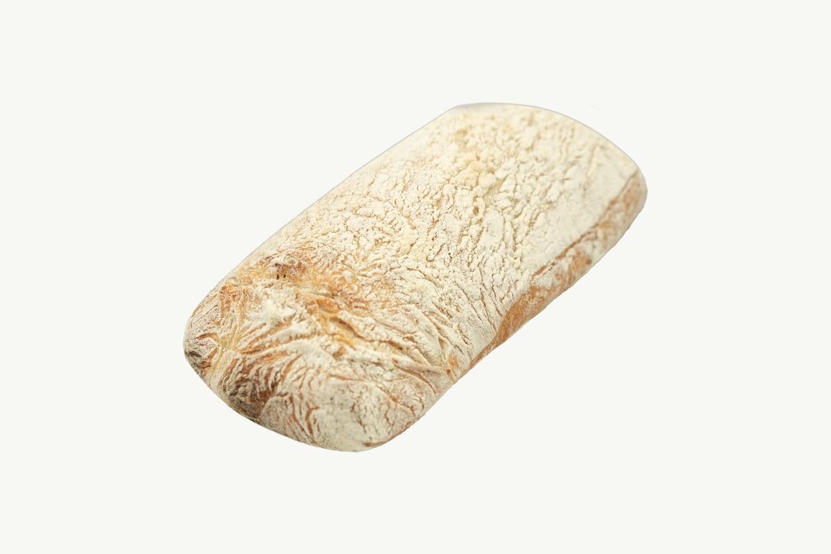 Flat open-crumbed sourdough ciabatta loaf resting on a plain cream surface